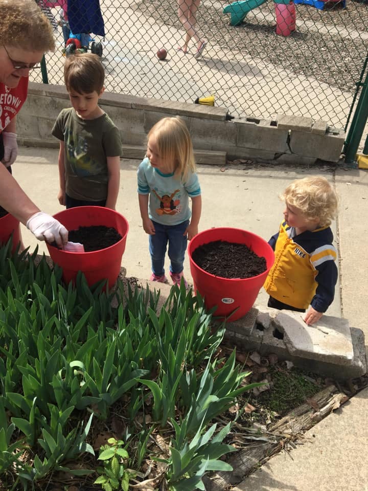Person and three children planting in red pots