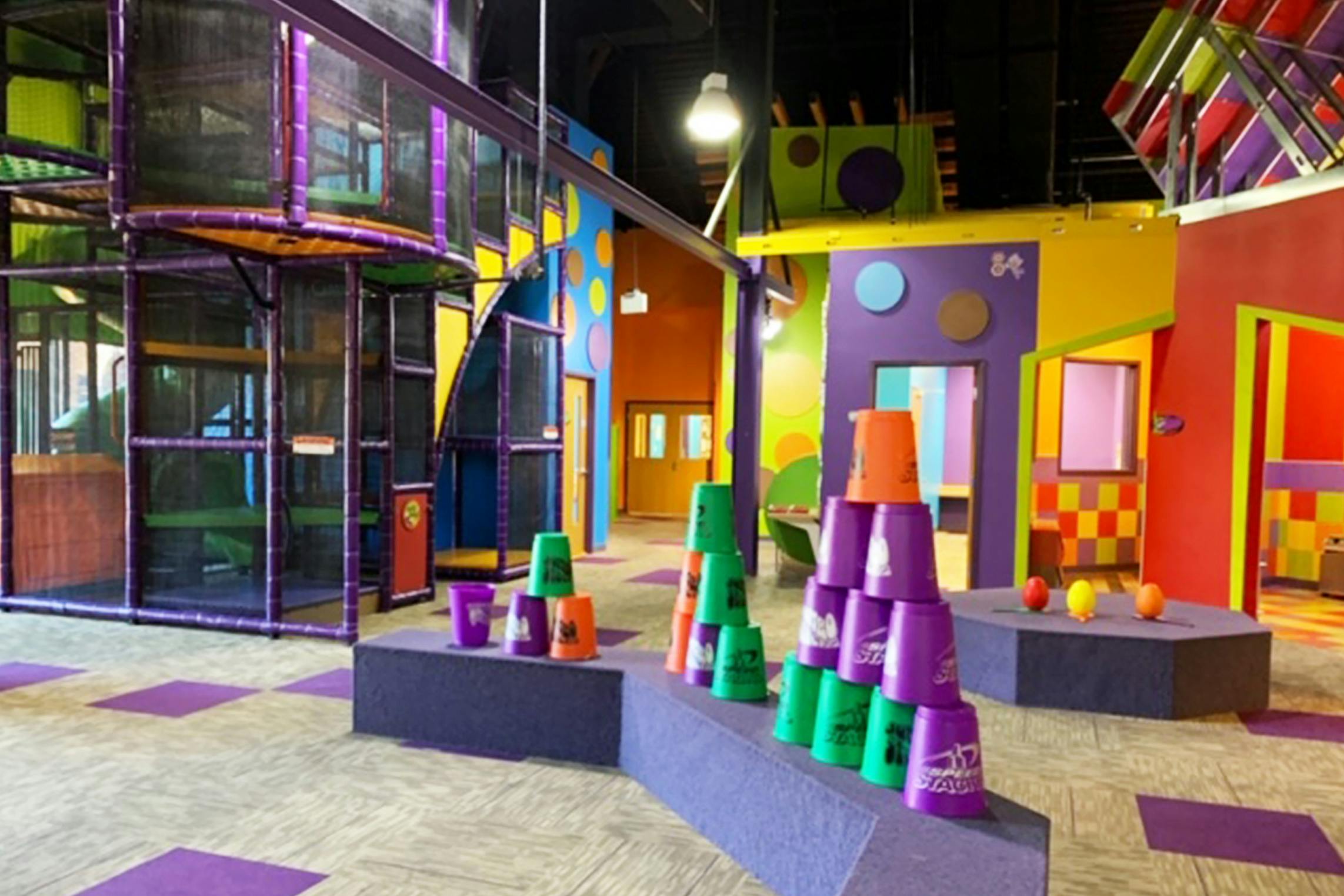 Colorful indoor children's play area with a large climbing structure and stacked cups