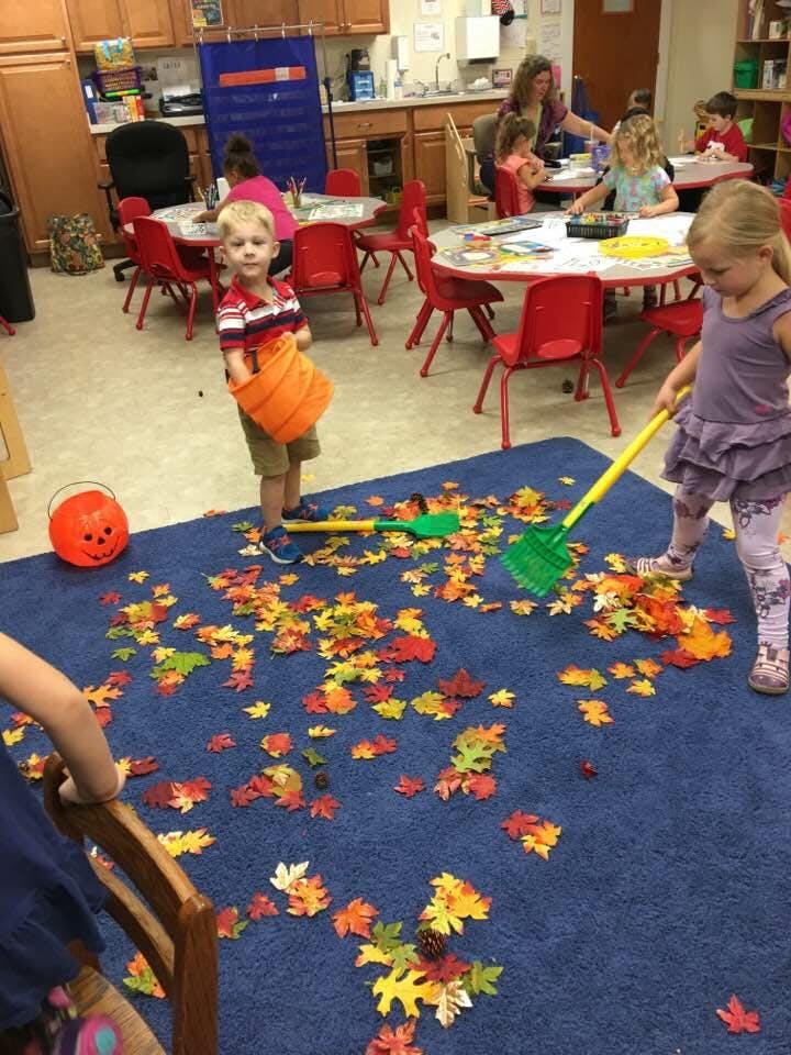 Children playing with toy leaves and shovels on a blue rug in a classroom