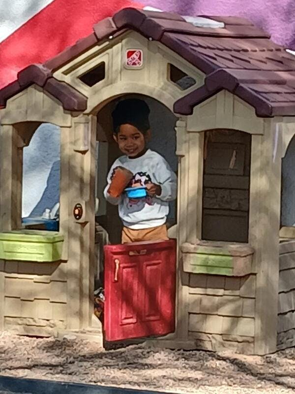 Child standing in a playhouse holding a cup and small bucket