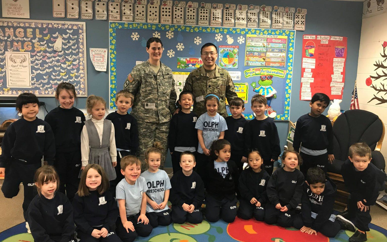 Two people in military uniforms standing with a group of children in a classroom