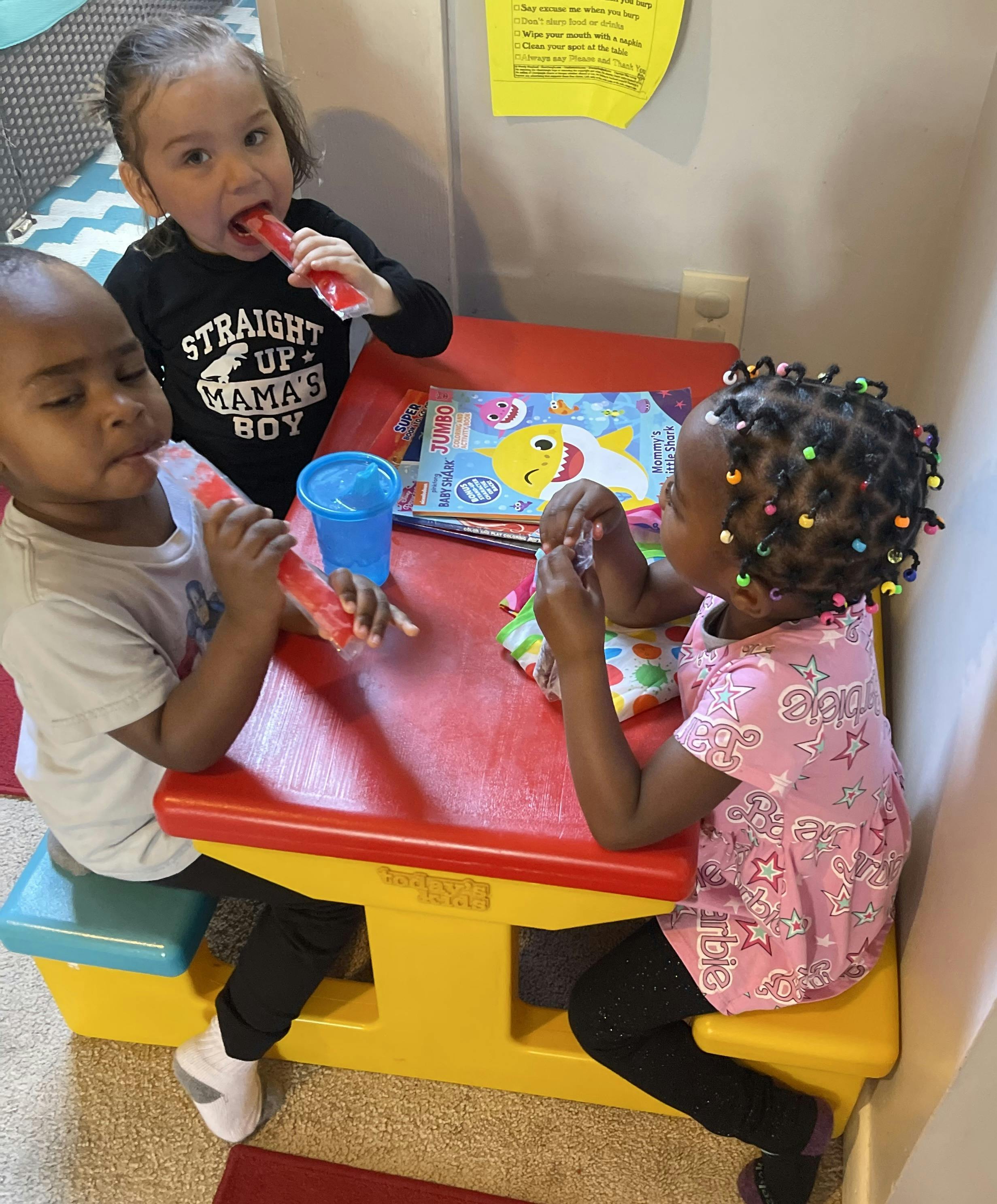Three children at a red table eating freeze pops