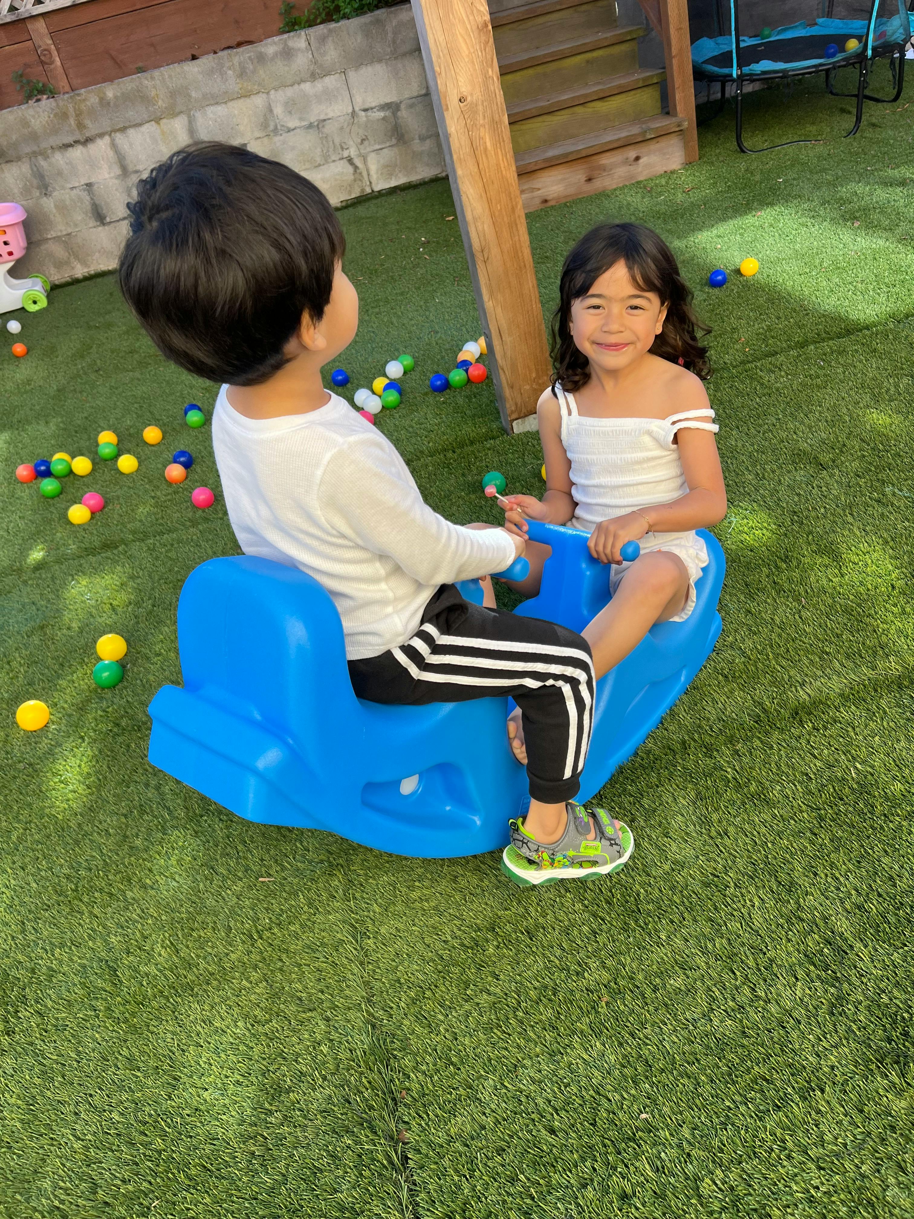 Two children on a blue seesaw toy on artificial grass