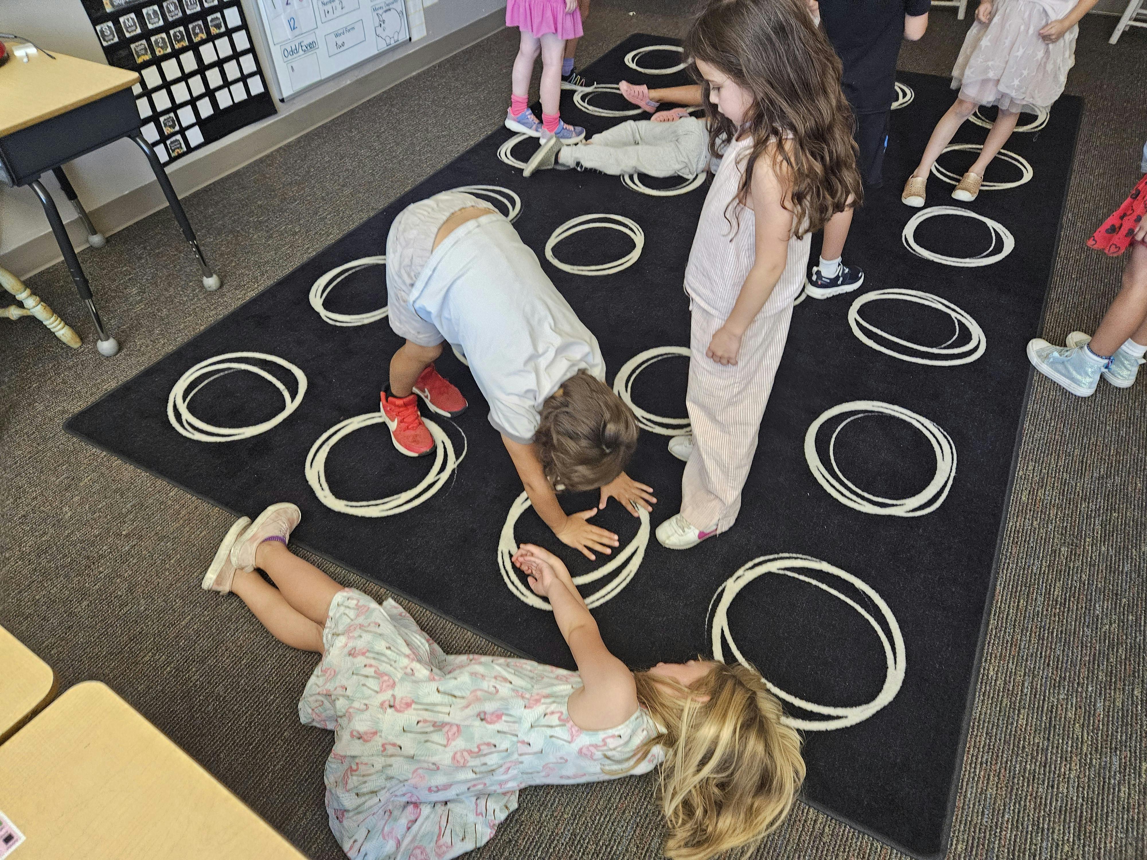 children playing on a black mat with white circles in a classroom