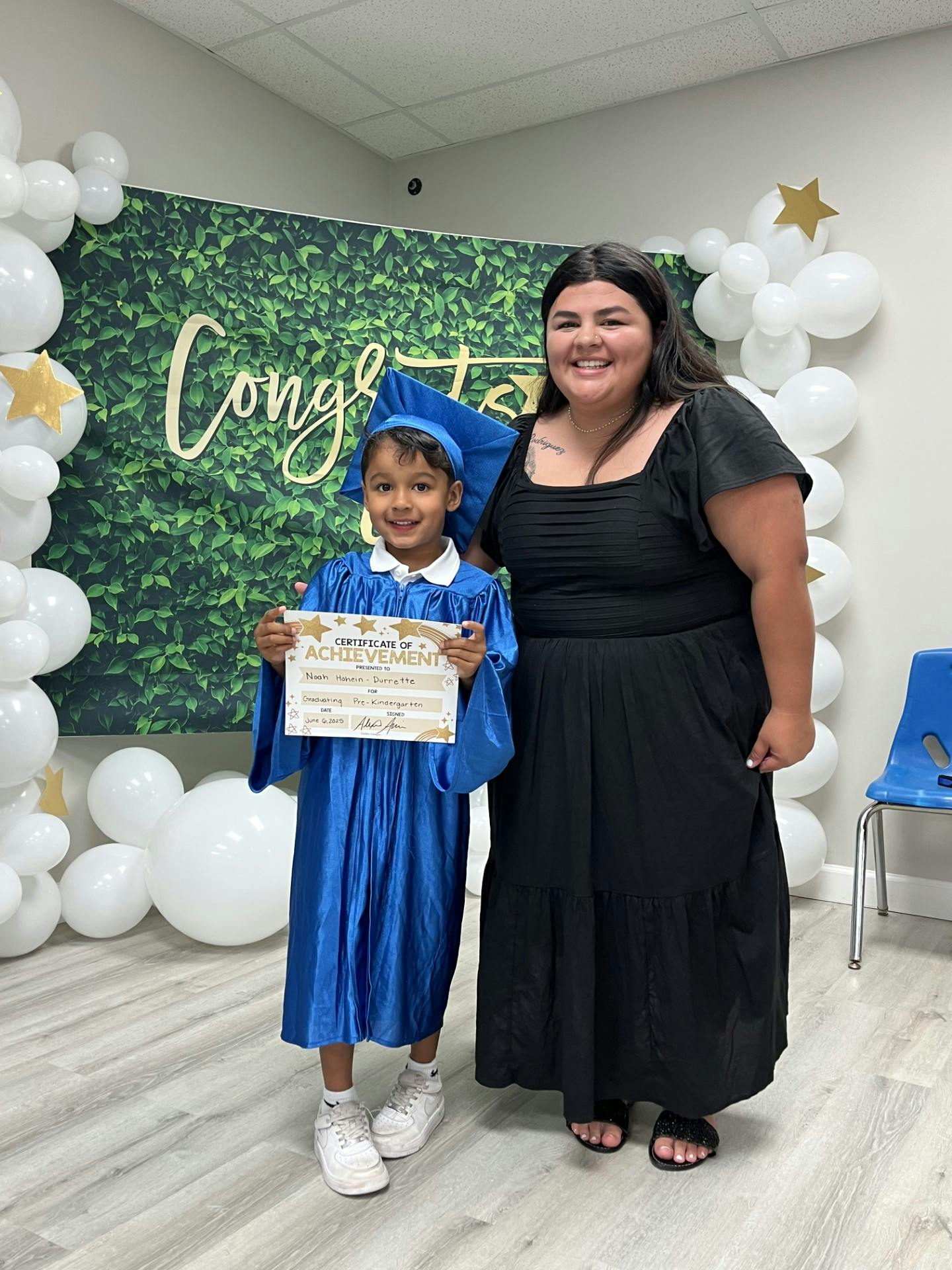 Child in blue graduation gown holding certificate next to an adult