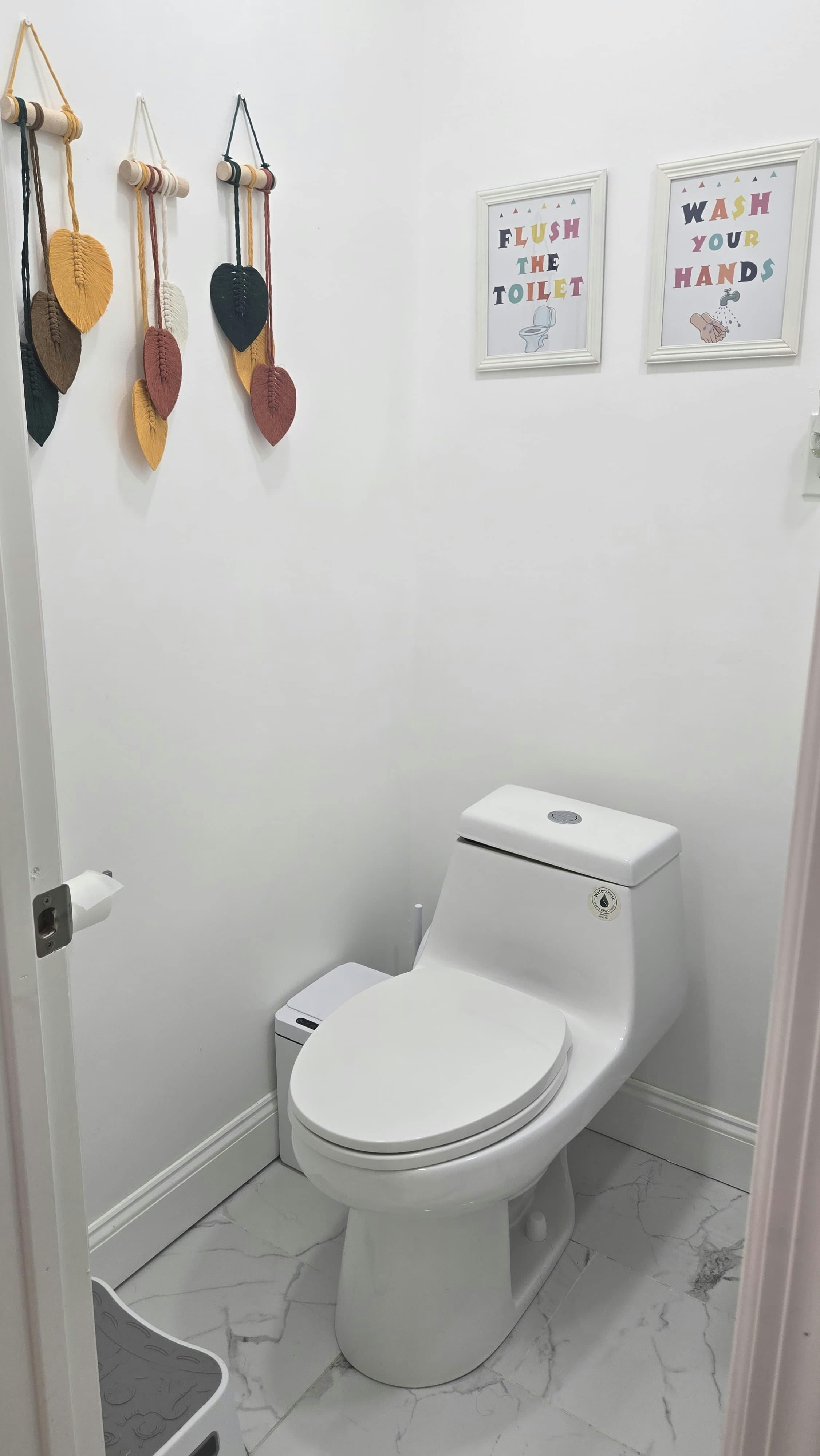 White toilet in a small bathroom with "Flush The Toilet" and "Wash Your Hands" signs
