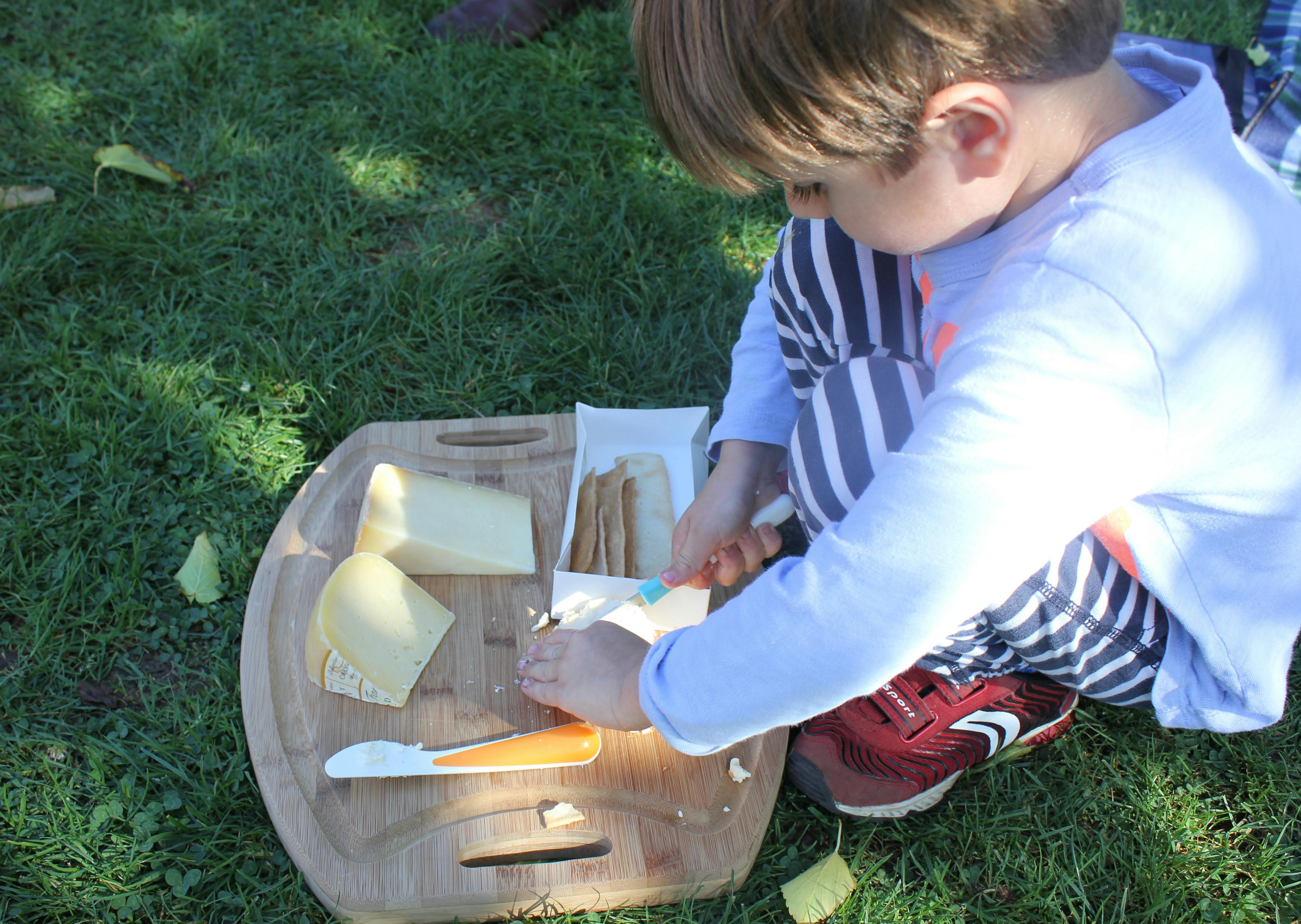 Child cutting cheese on a wooden board outdoors