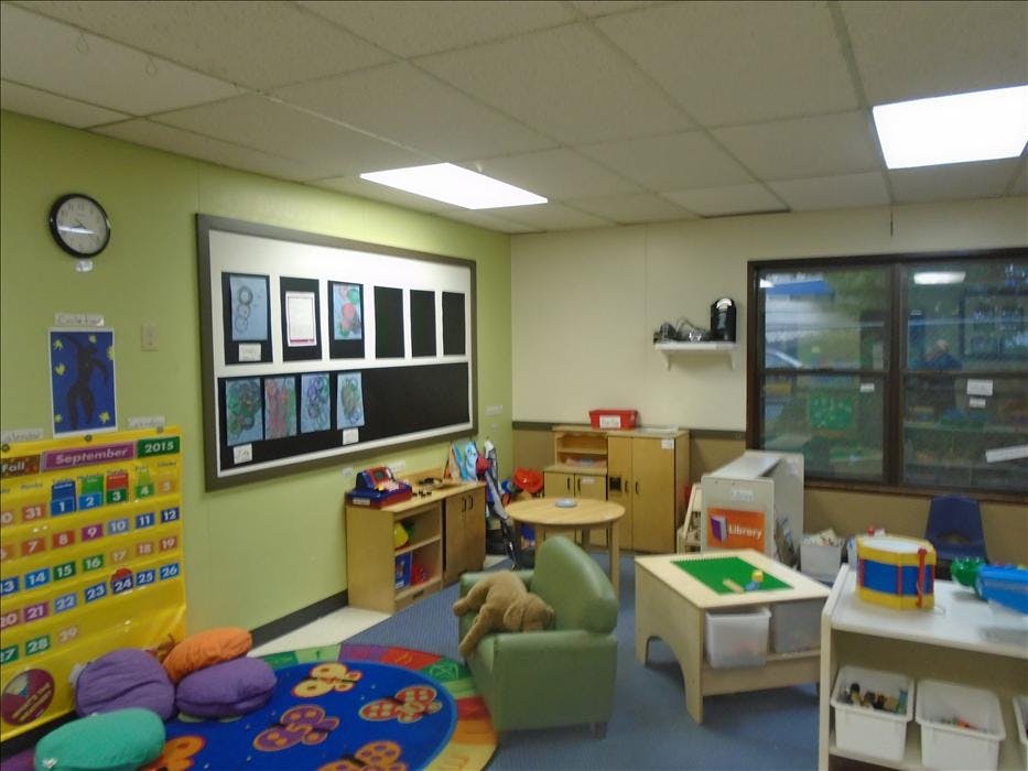 A classroom with a calendar, child artwork, tables, chairs, and shelves