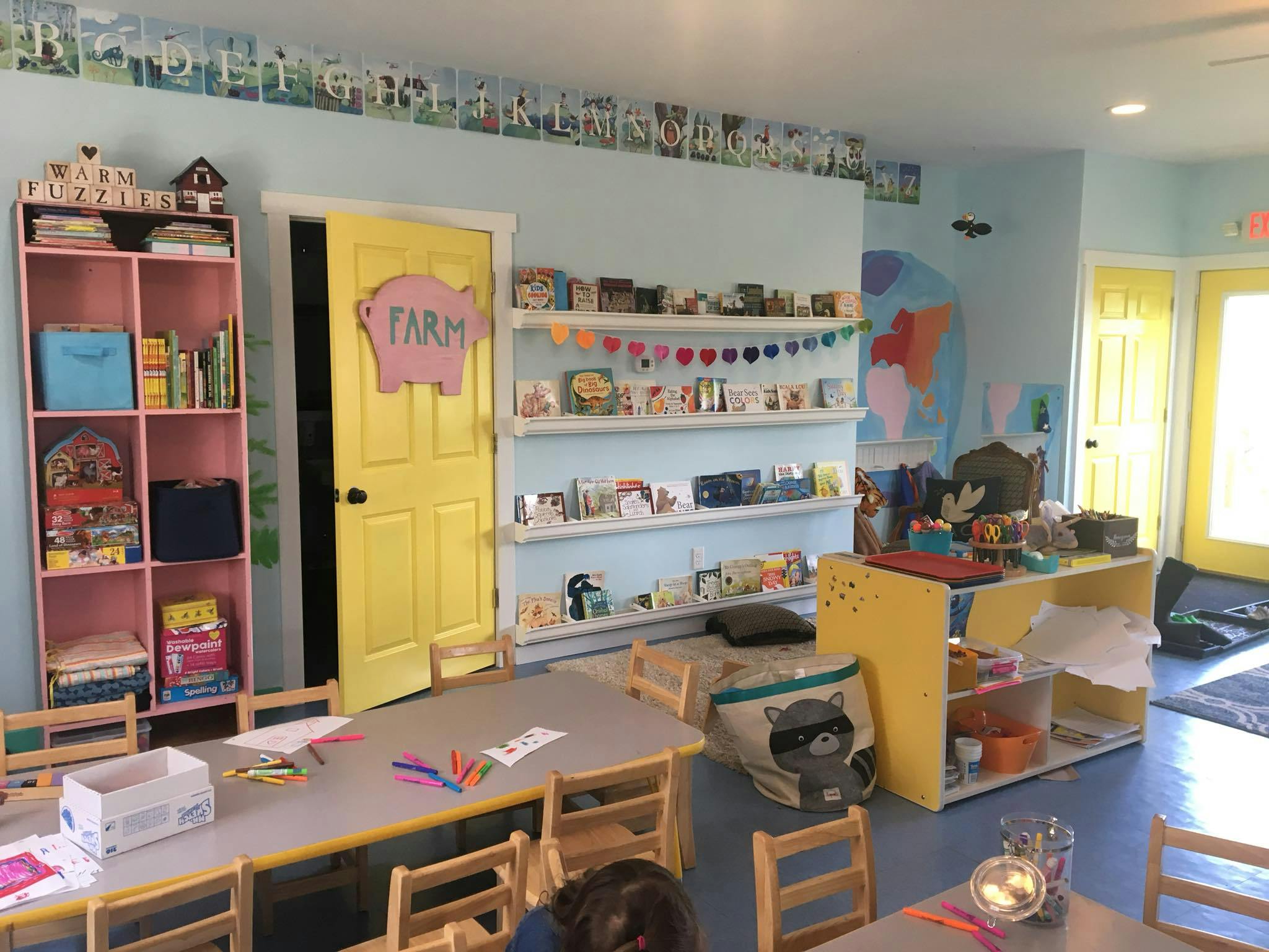 Classroom with tables, chairs, shelves of books, and a yellow door with "FARM" sign
