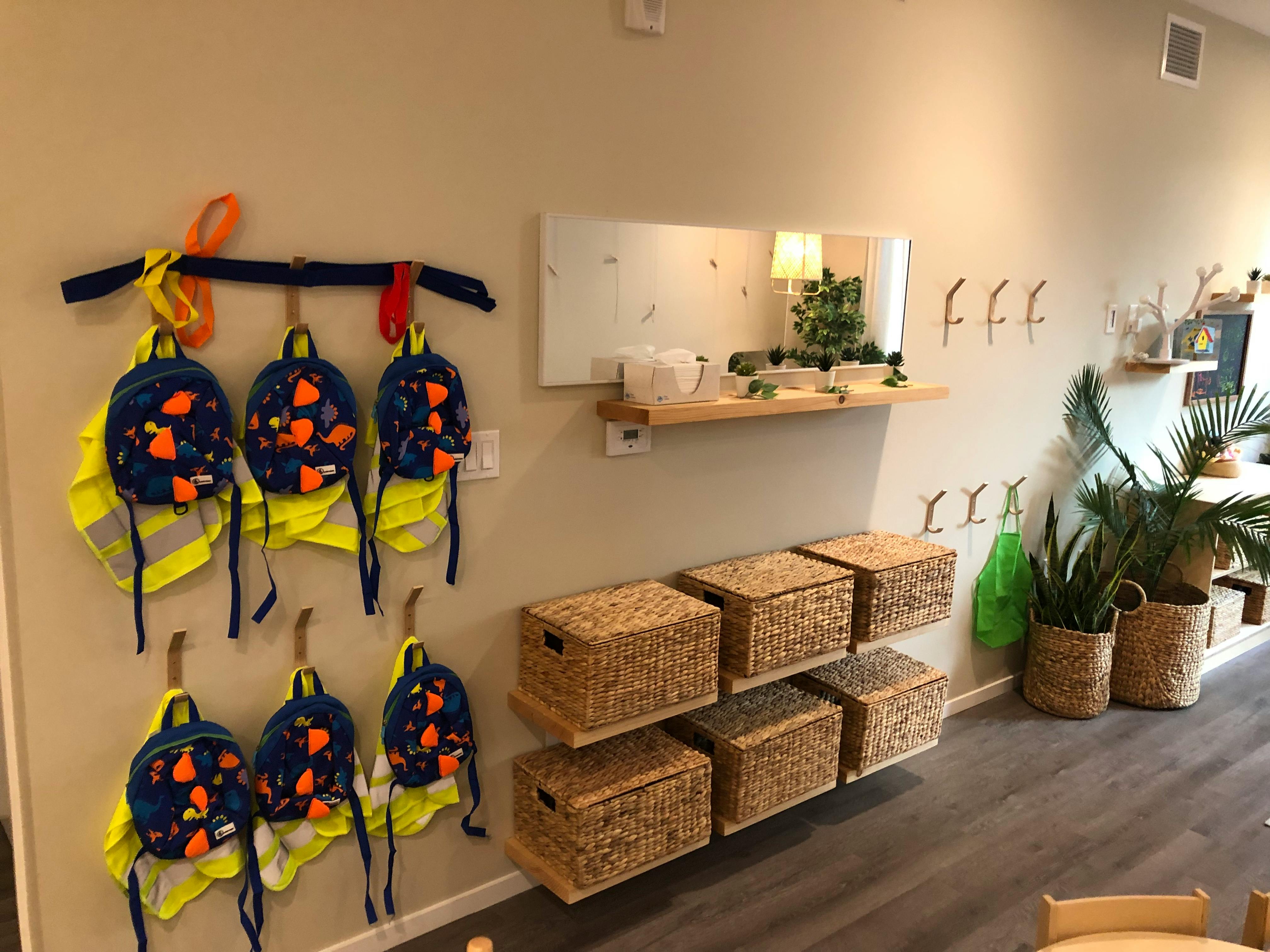 Backpacks and safety vests hanging on a wall next to wicker storage baskets