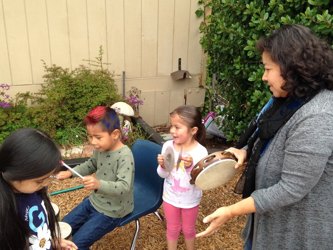 Adult and three children playing musical instruments outdoors
