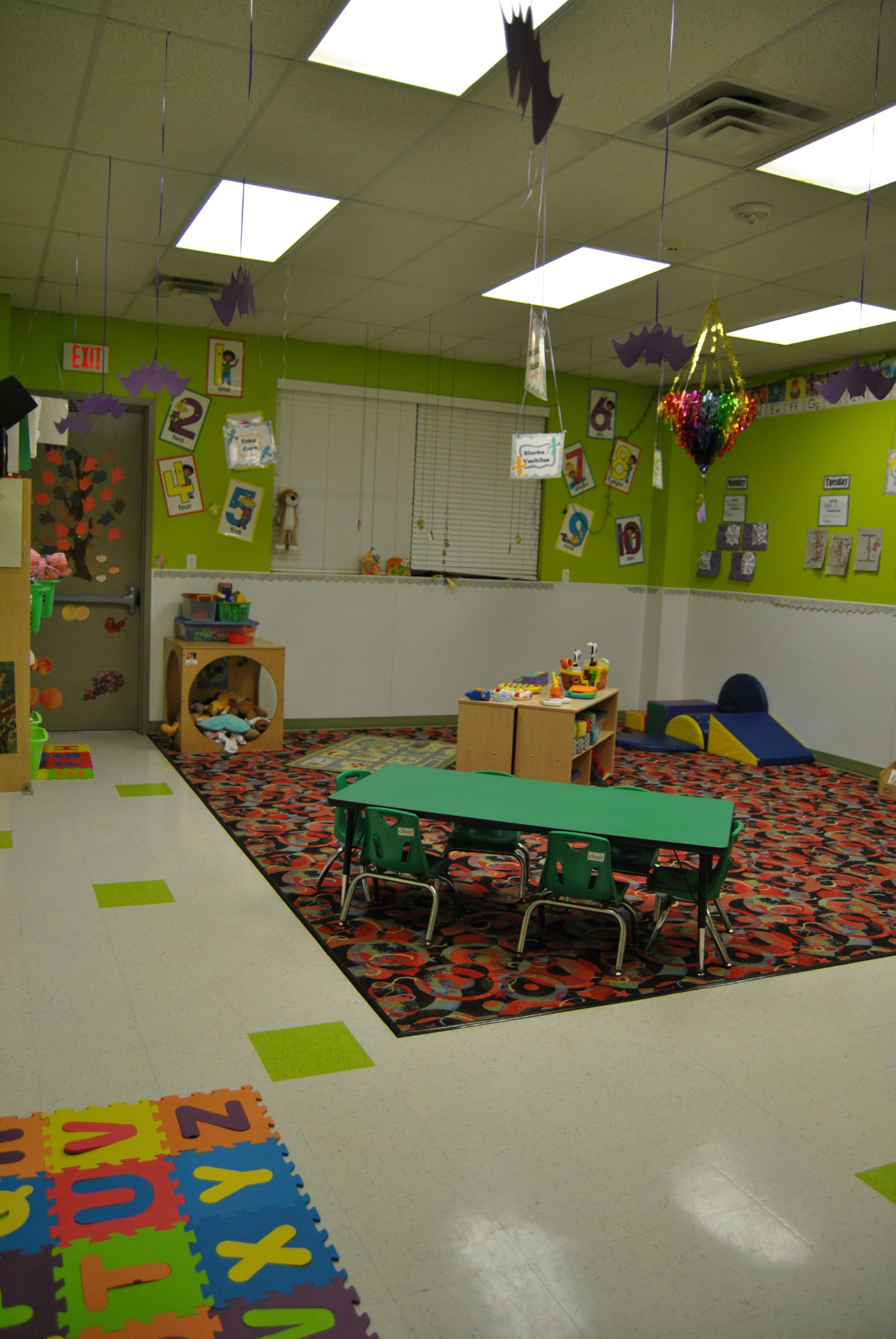 A classroom with green walls, a colorful rug, and small tables and chairs