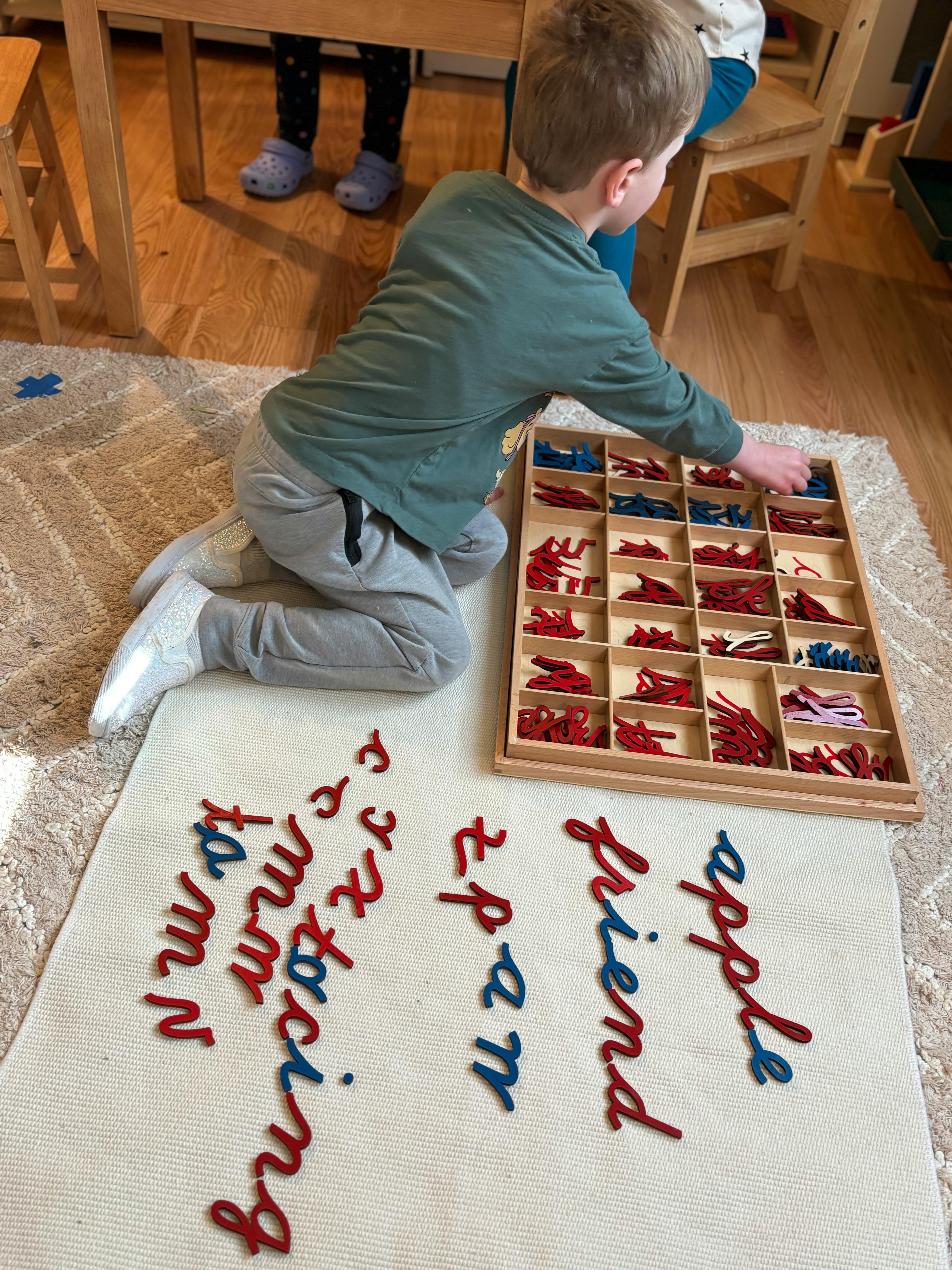 Child on floor selecting letters from a tray to form words on a mat