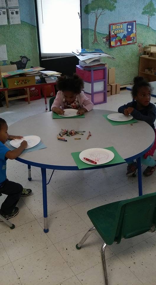 Three children drawing at a round table in a classroom