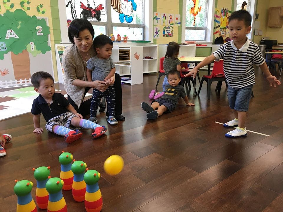Adult and children playing with bowling pins and a ball in a classroom