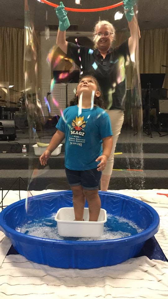 Person making a large bubble around a child standing in a pool