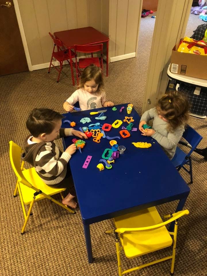Three children playing with colorful toys at a blue table