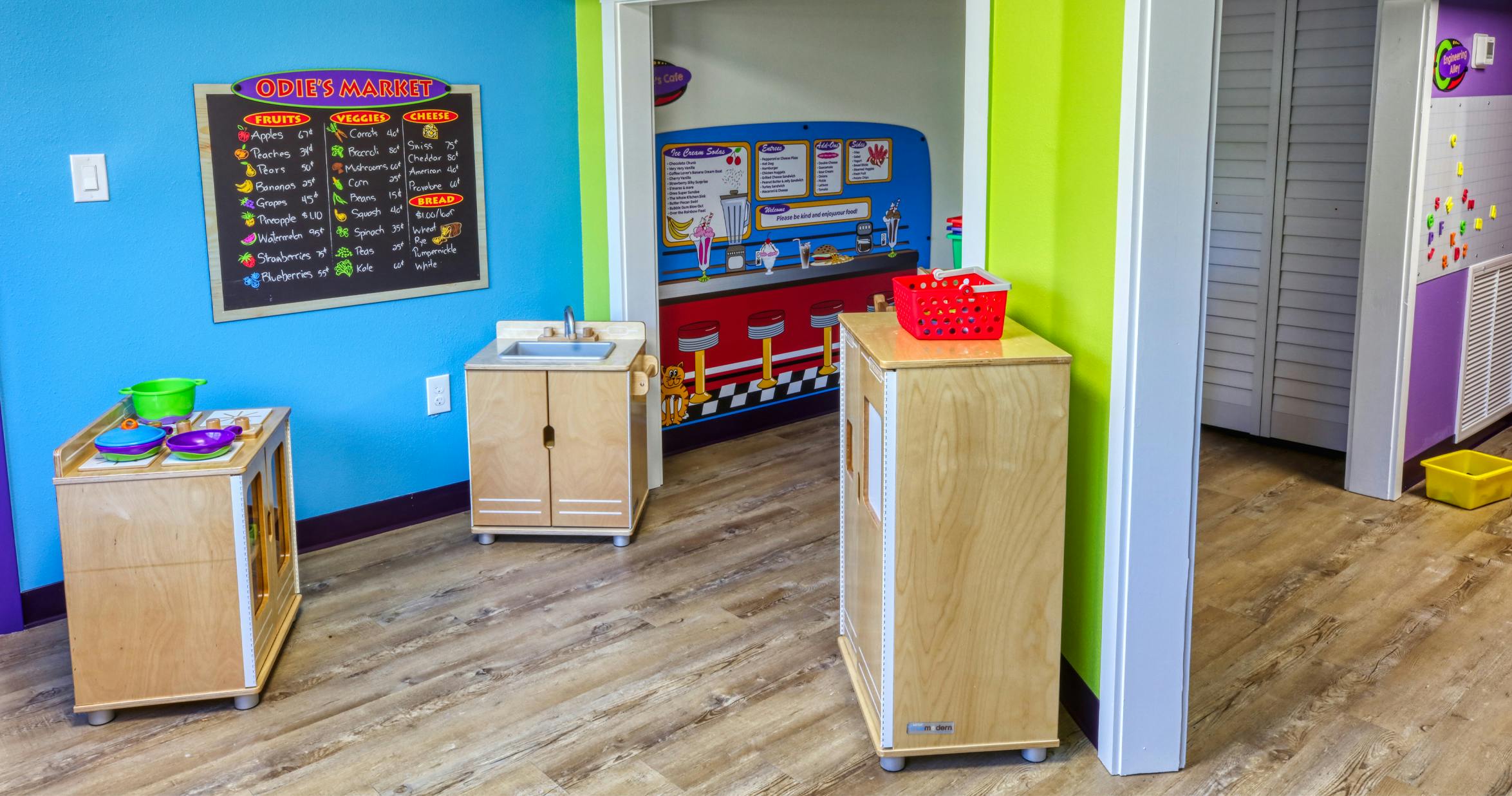 Play kitchen with sink and stovetop next to a market chalkboard