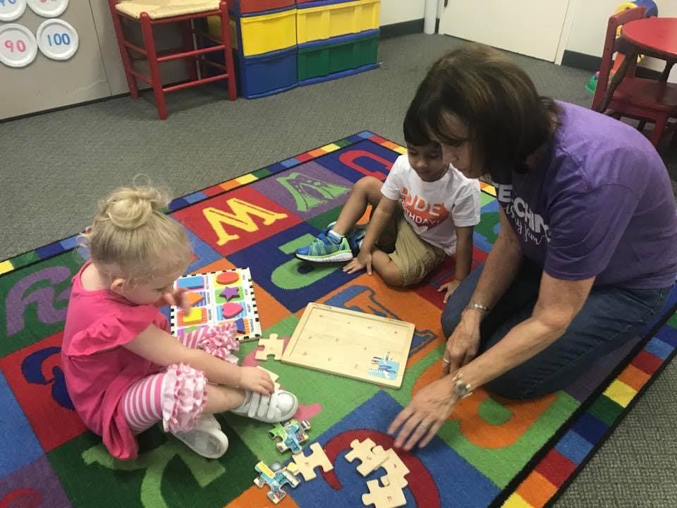 Adult and two children playing with puzzles on a colorful alphabet rug