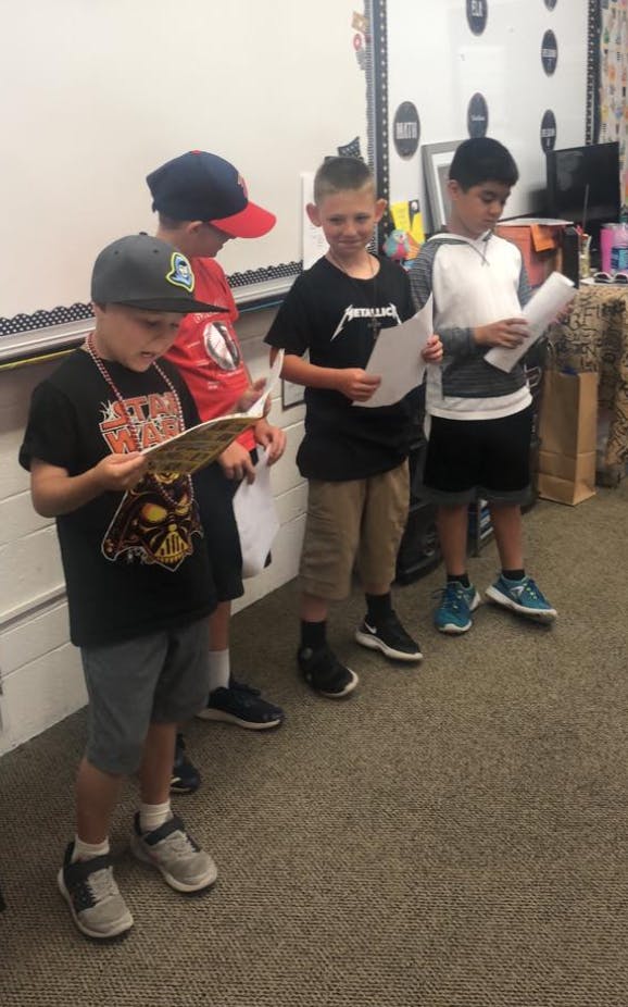 Four children standing and looking at papers in a classroom