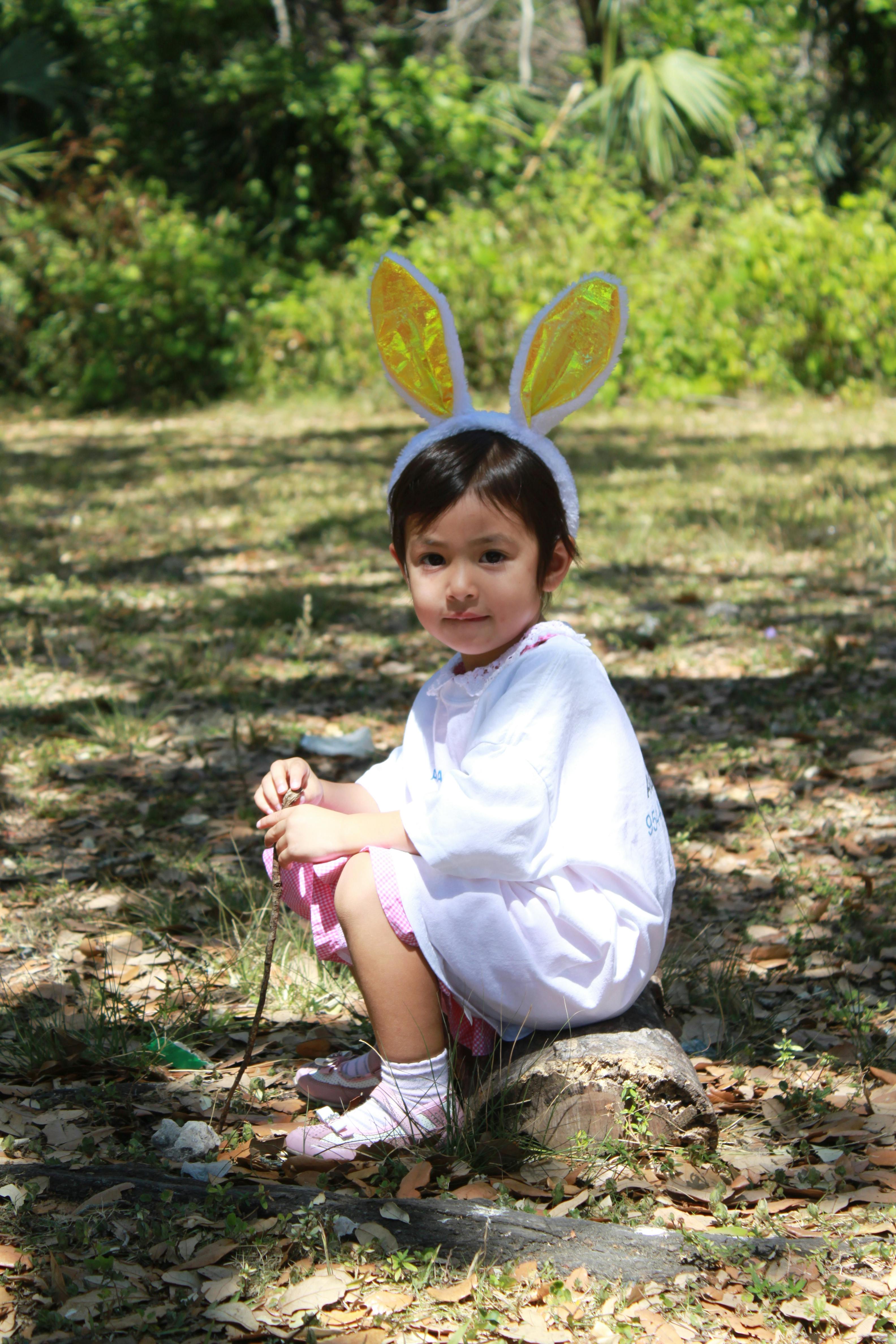 Child wearing bunny ears sitting on a tree stump outdoors