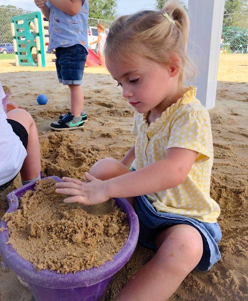 Child playing in sand with a purple bucket