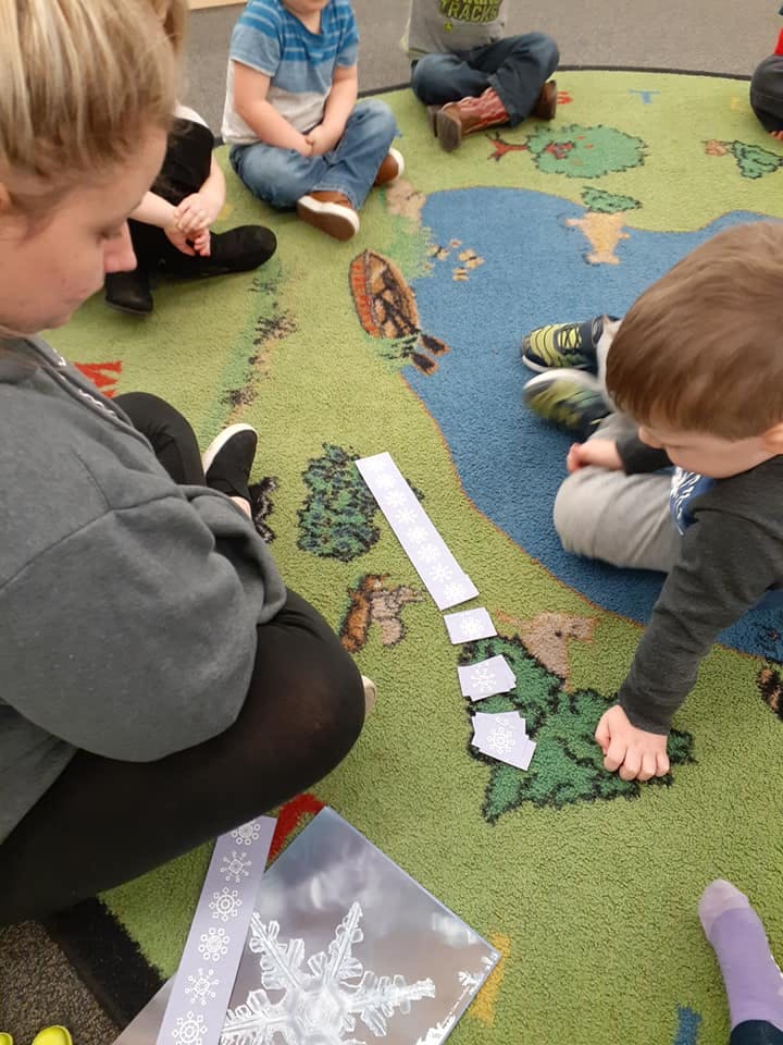 Person and child on a rug with a map design, child playing with paper pieces