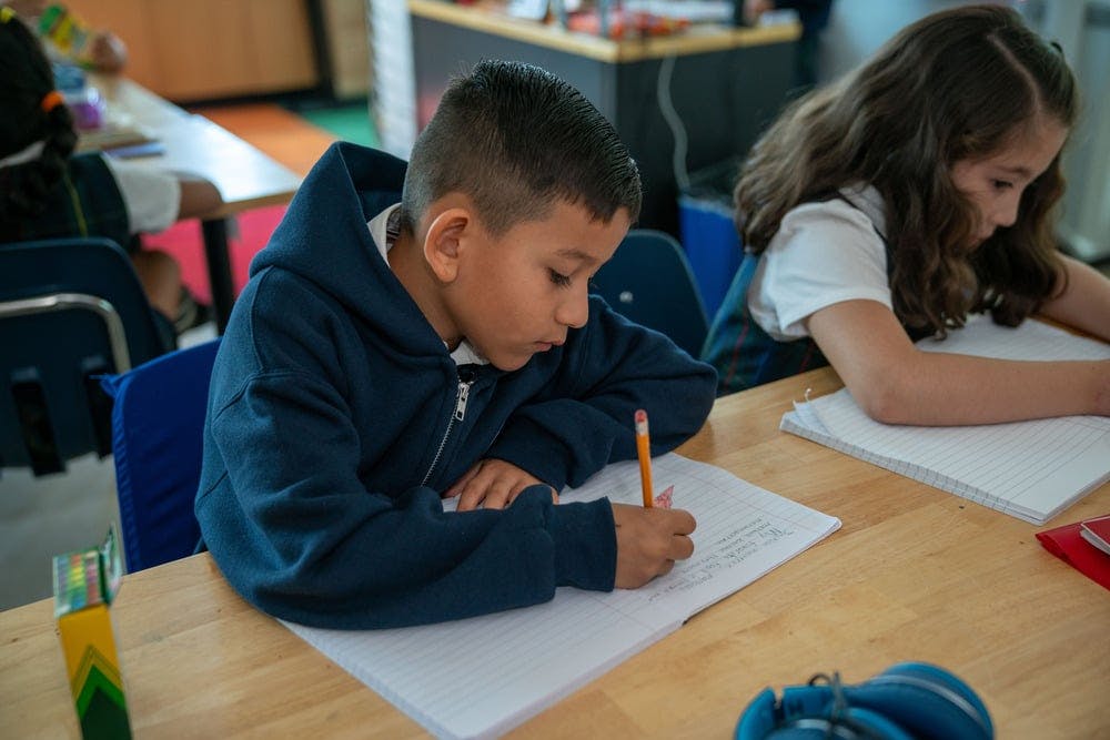 Child writing in a notebook at a desk in a classroom