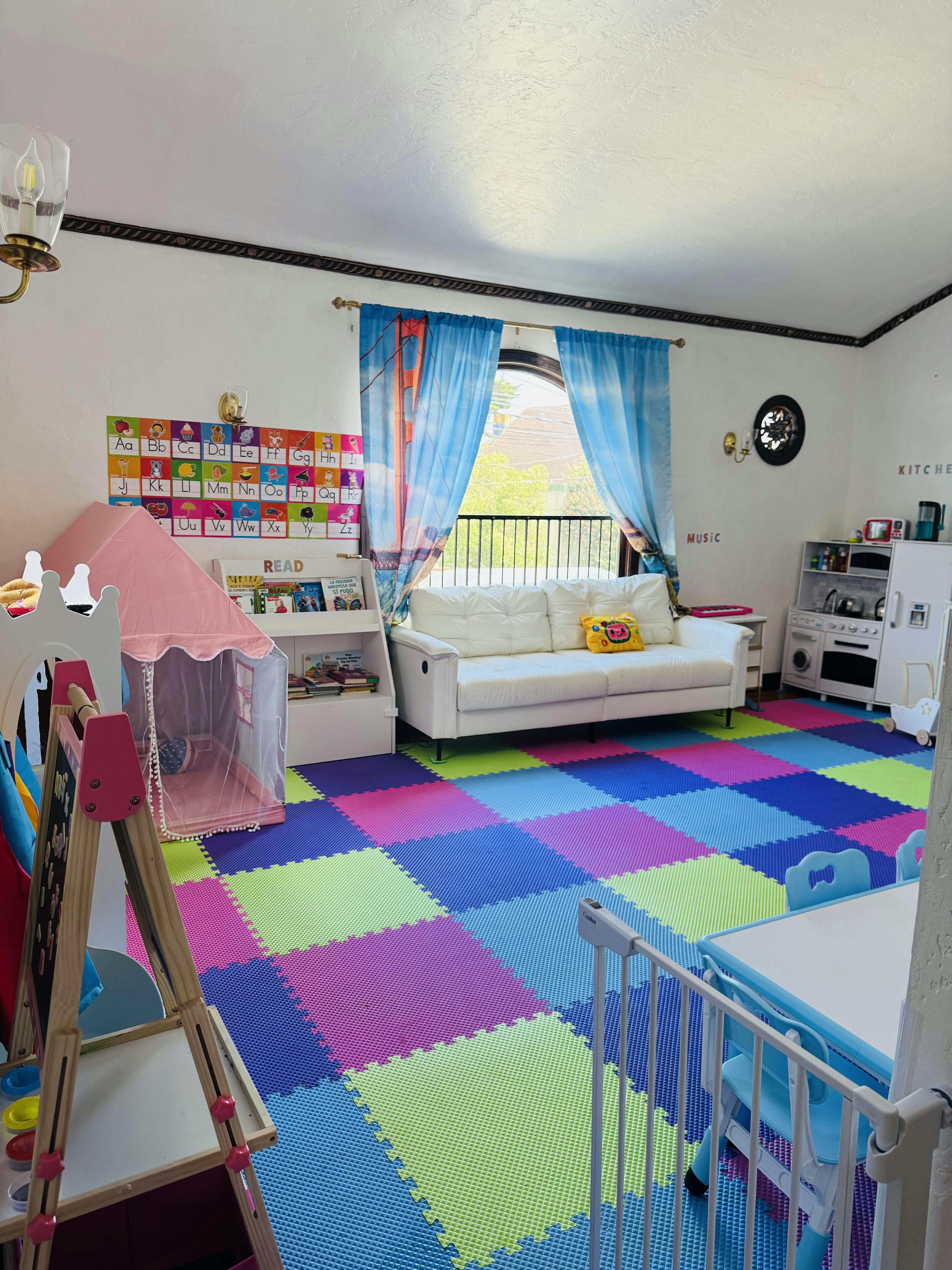 Playroom with colorful interlocking floor mats, a white sofa, and a pink tent