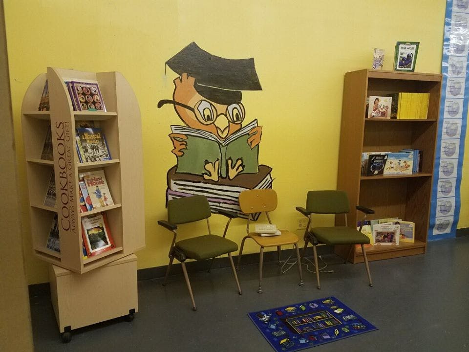 Book display, bookshelf, and chairs in a room with an owl mural
