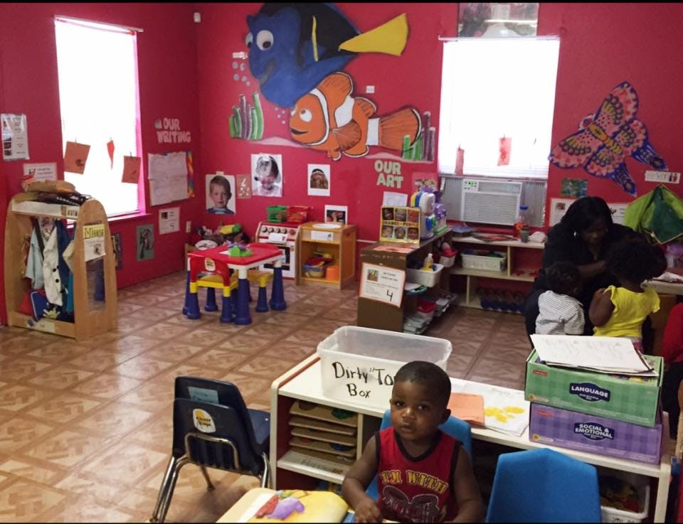 Child sitting at a table in a classroom with another person and child