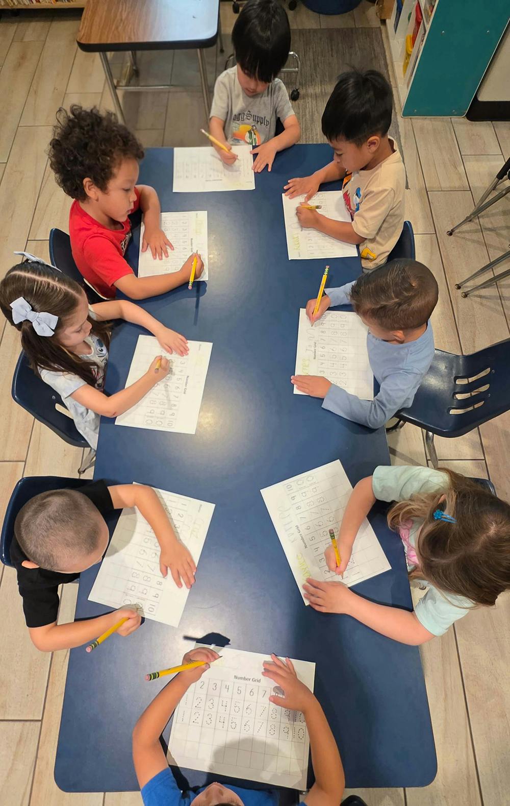 Group of children at a table filling out number grid worksheets