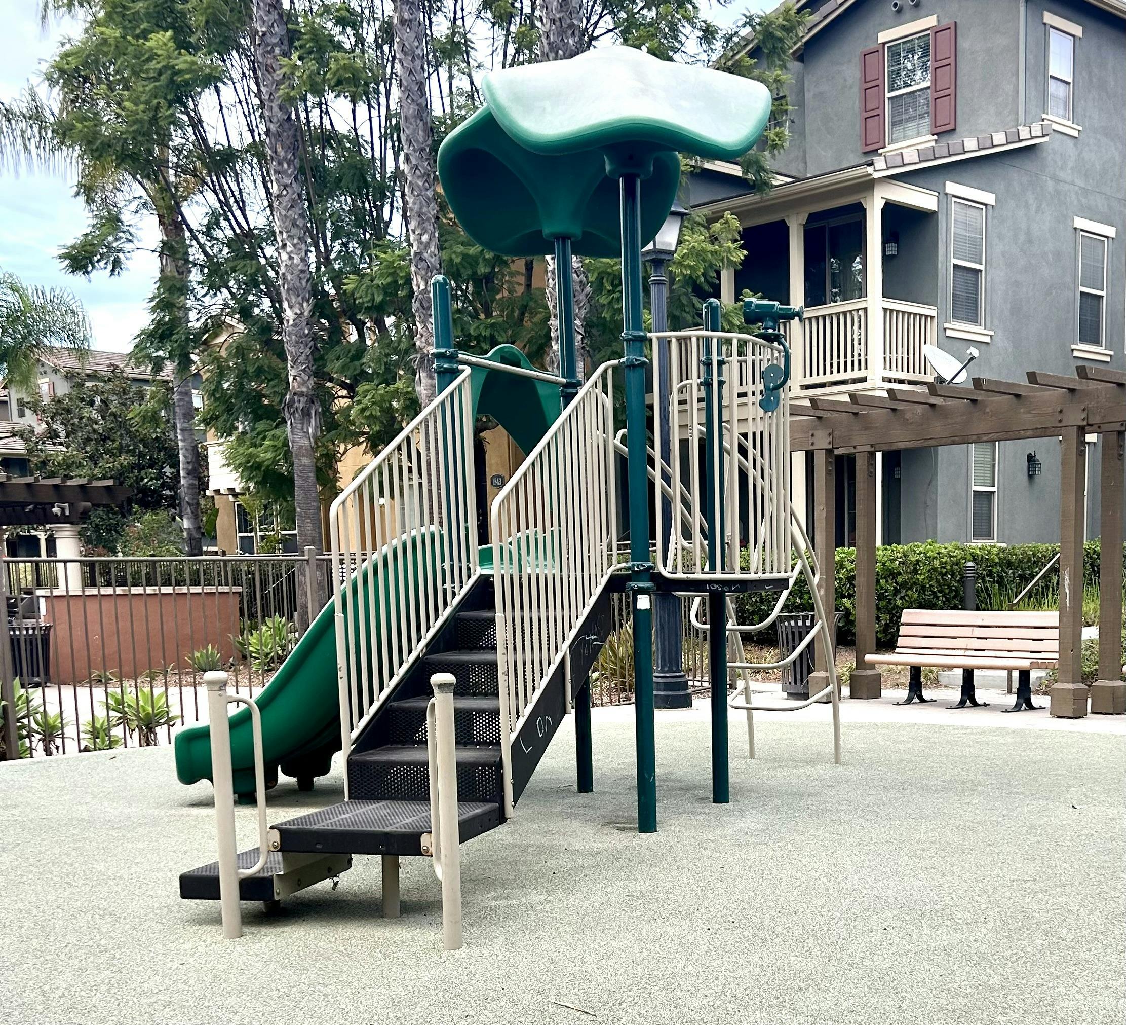 Empty playground with green slides and a nearby park bench