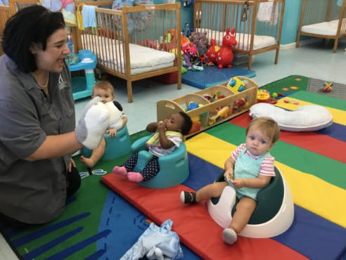 Person interacting with three children in a room with cribs
