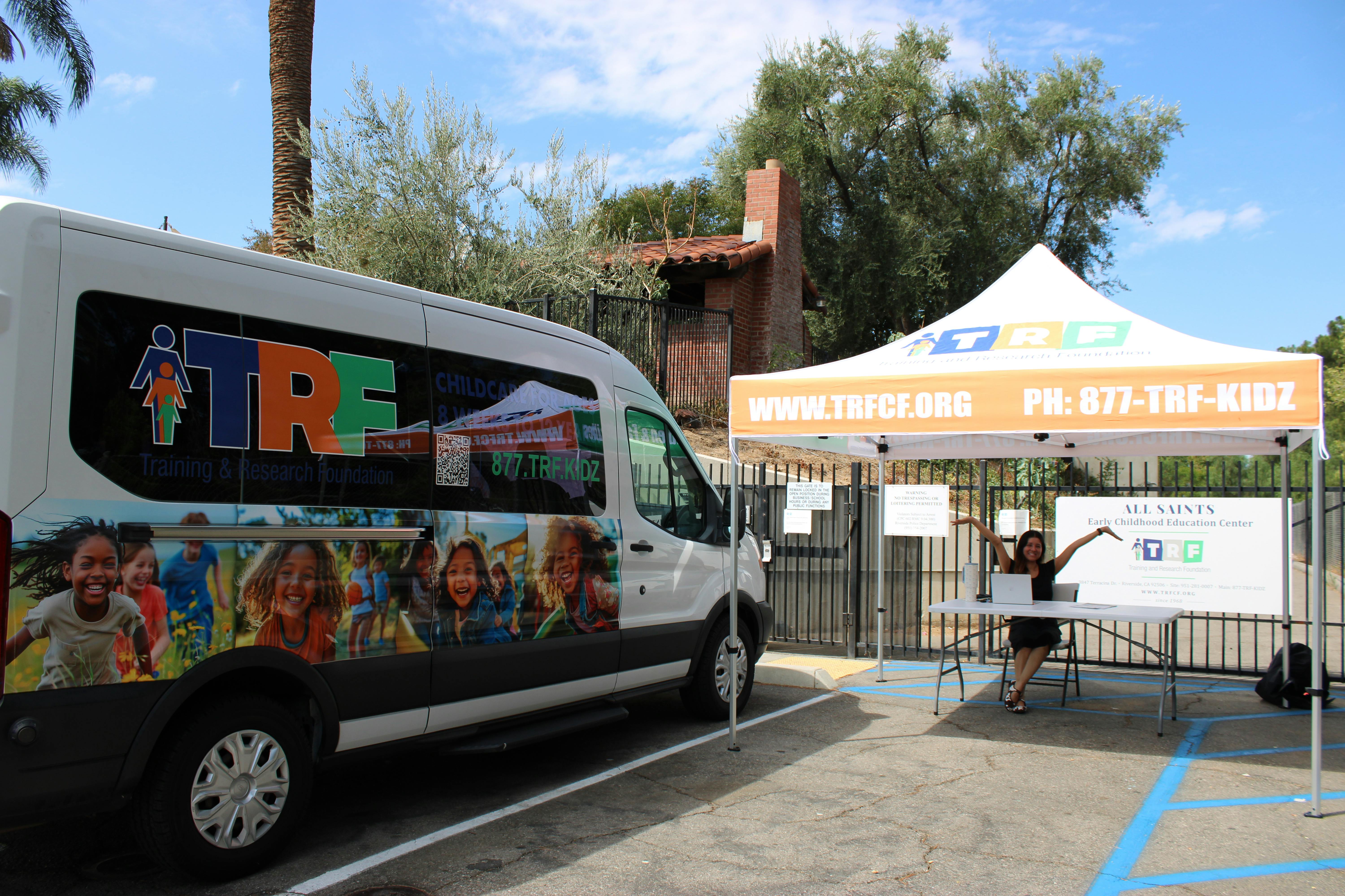 van with TRF logo and children's faces, tent, and person at a table