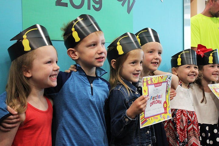 Group of children wearing graduation caps, one holding a diploma