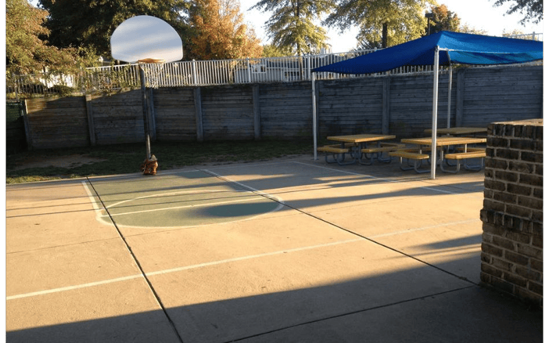 Basketball hoop on a court with picnic tables under a blue canopy