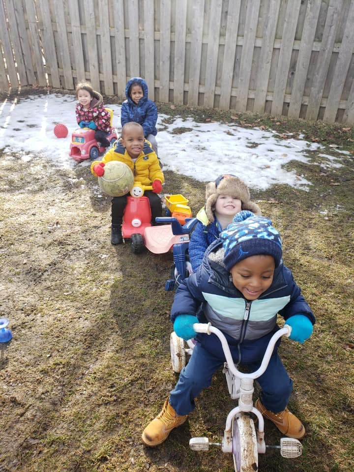 Children riding toy vehicles outdoors in a line