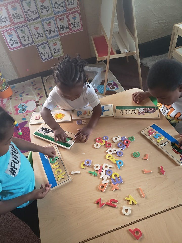 Three children playing with alphabet puzzles and letters at a table