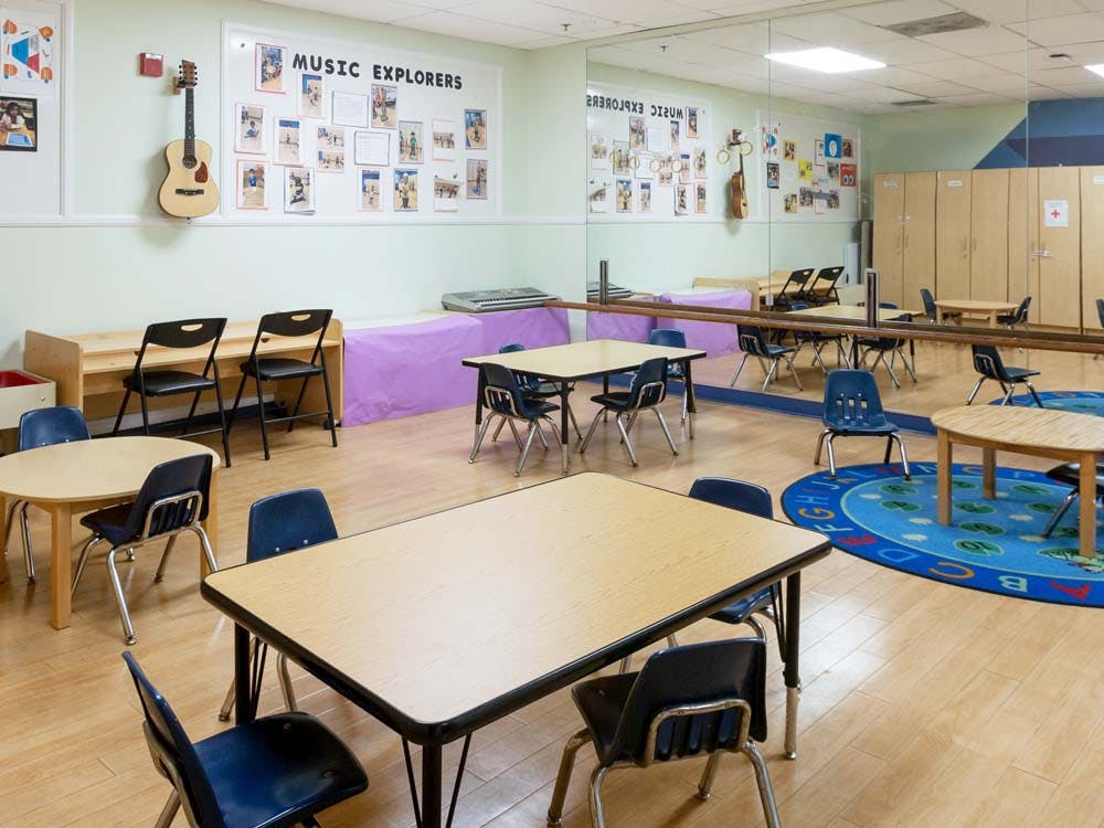 Classroom with tables and chairs, a mirror, and a sign reading "MUSIC EXPLORERS"