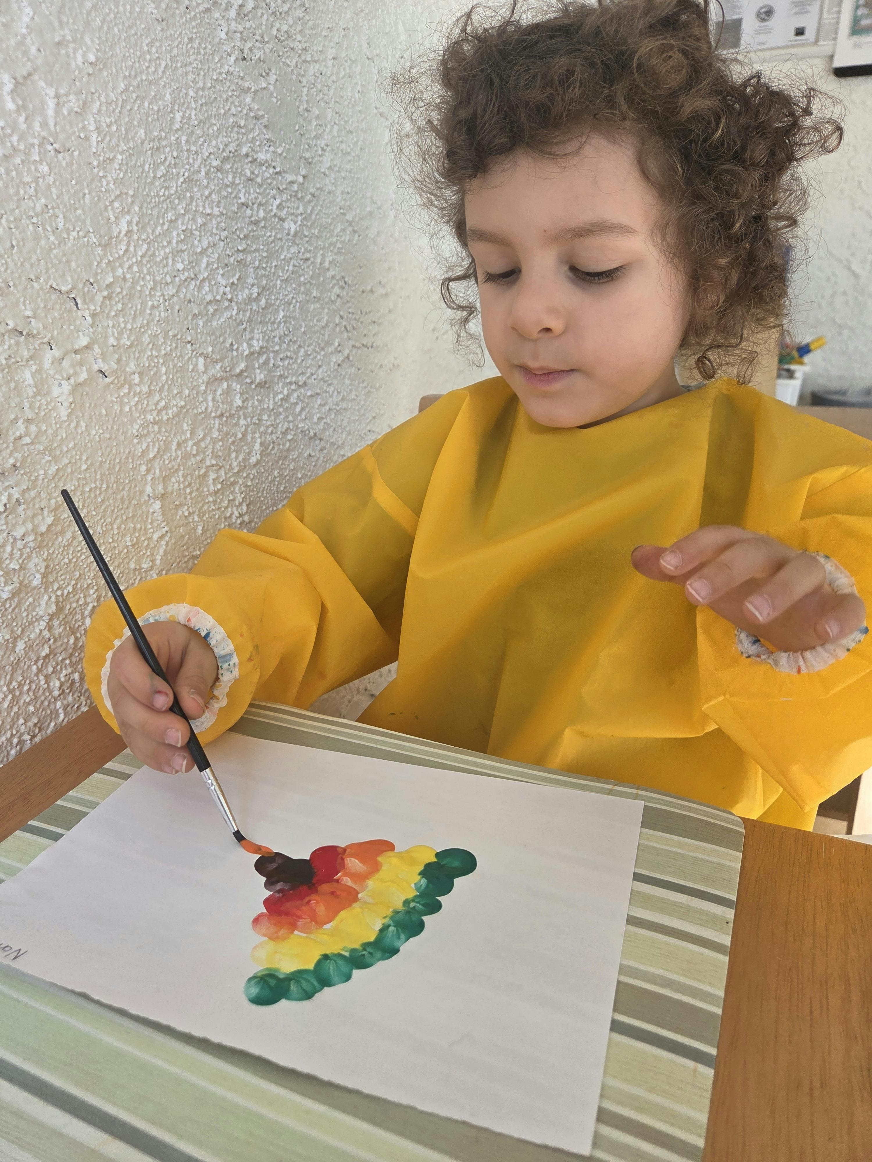 Child in yellow smock painting with a brush