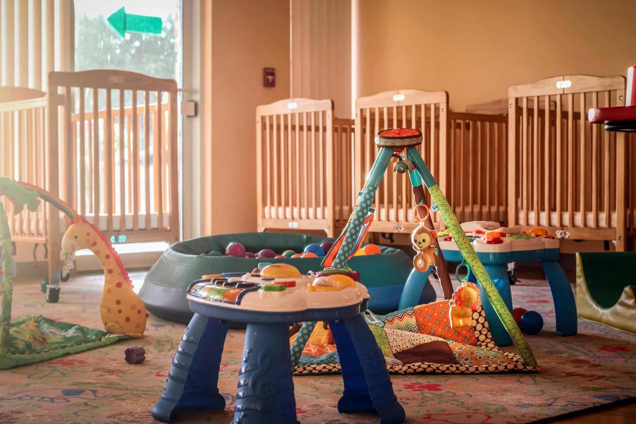 Nursery room with multiple cribs and various infant toys on the floor