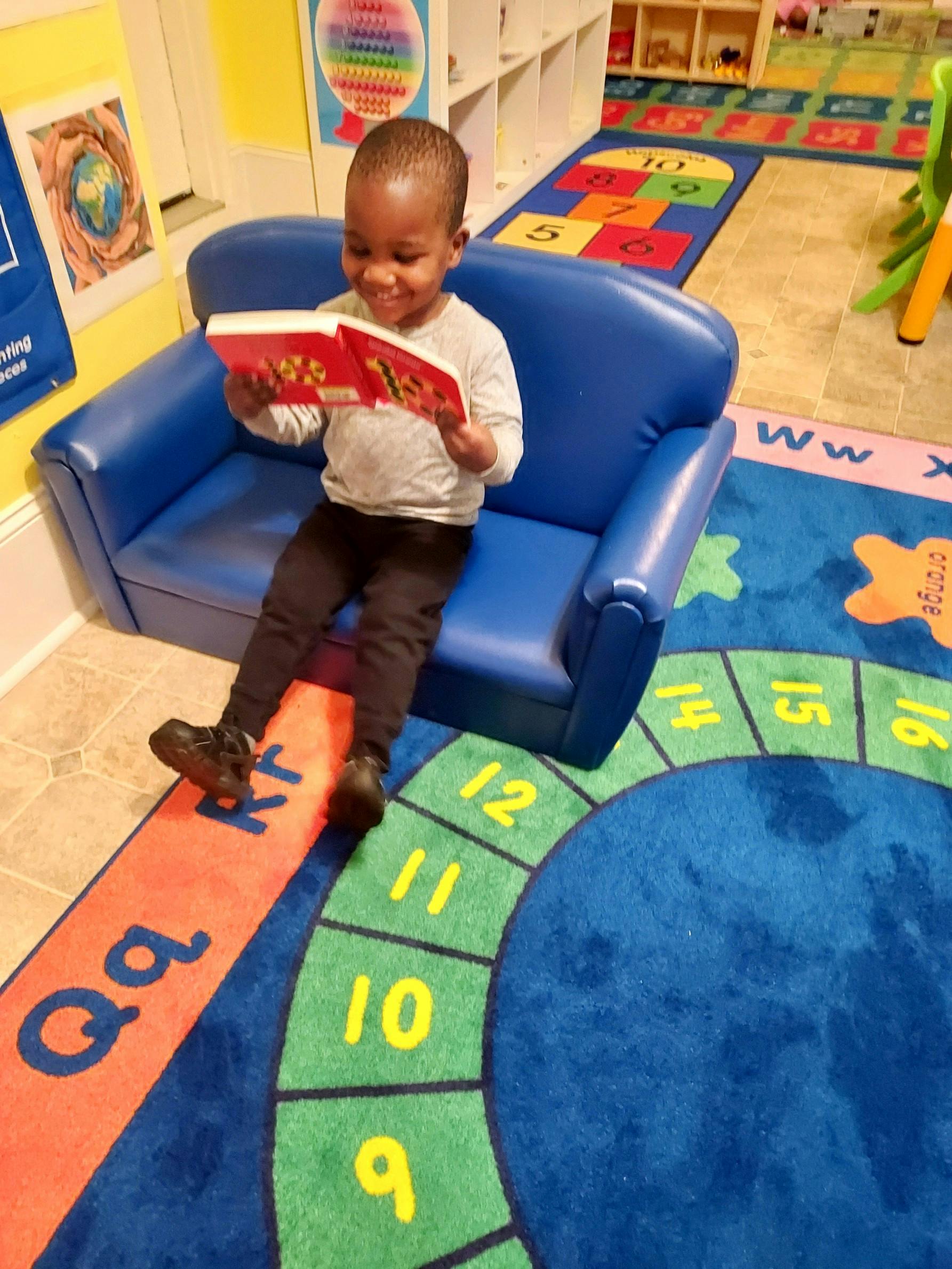 Child sitting on a blue couch reading a book in a classroom