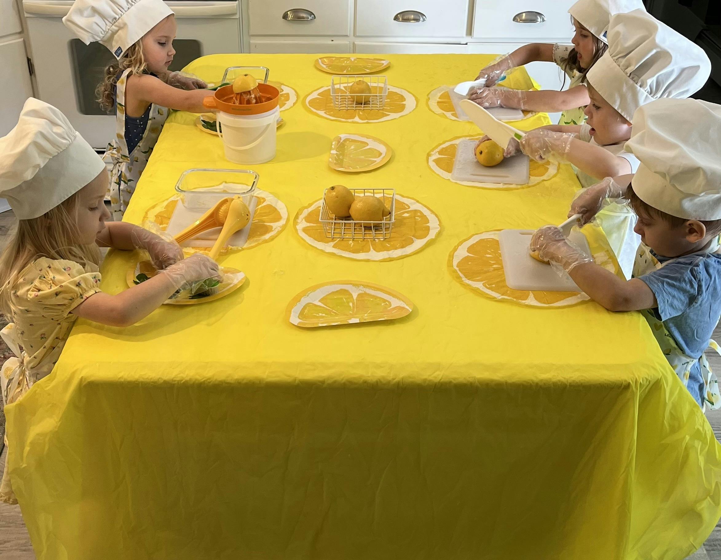 Children wearing chef hats preparing lemons at a table