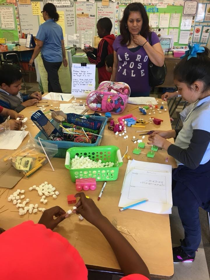 People and children working on crafts at a table in a classroom