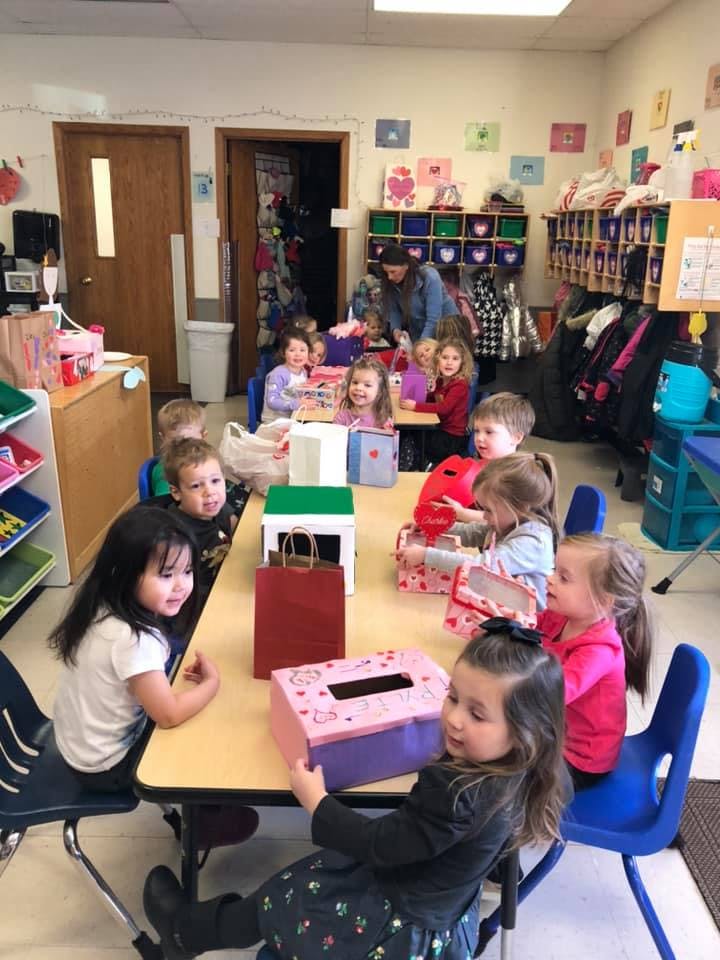 Children sitting at tables in a classroom with gift bags and craft items