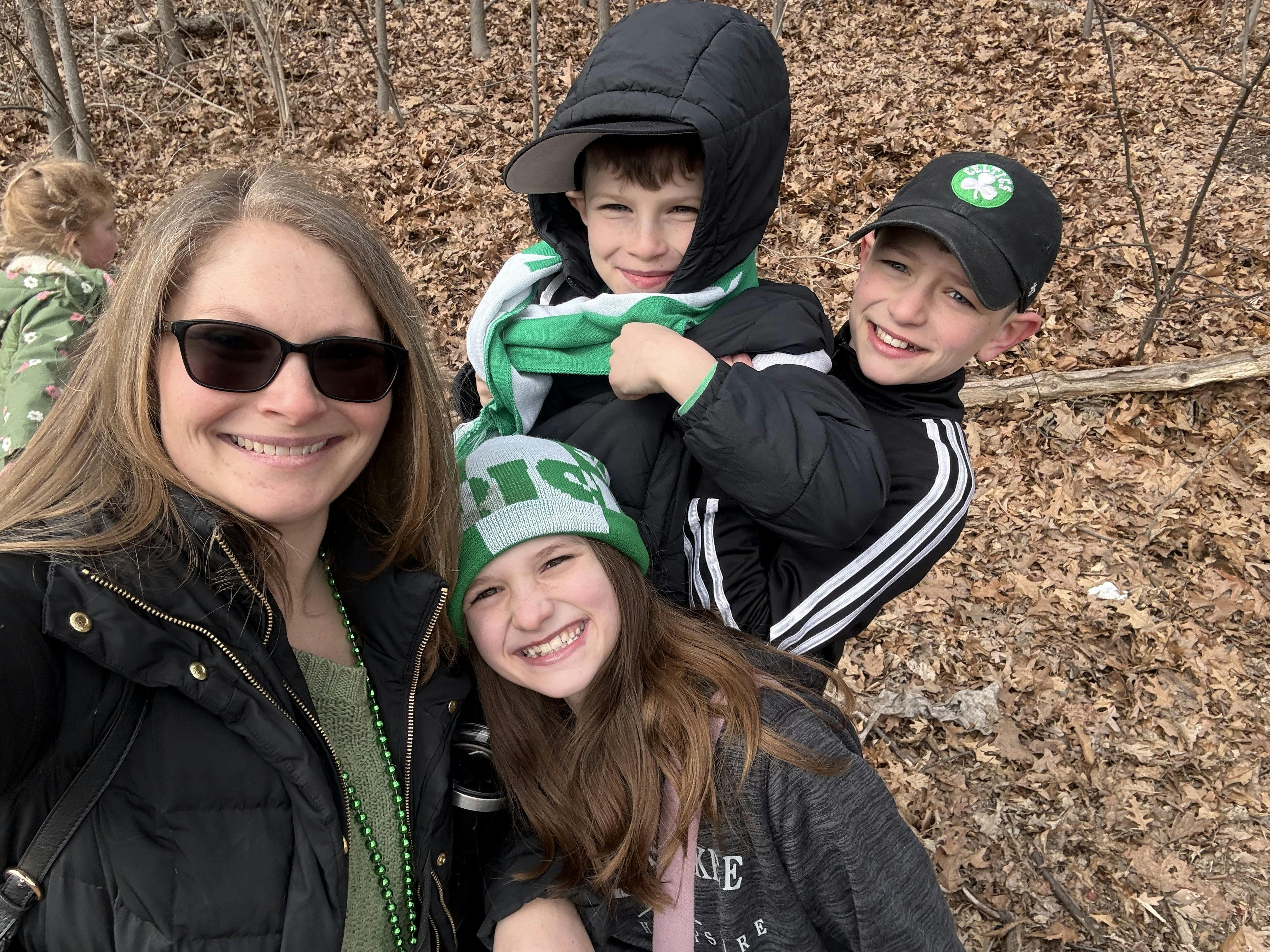 A person and three children posing for a photo outdoors in a wooded area