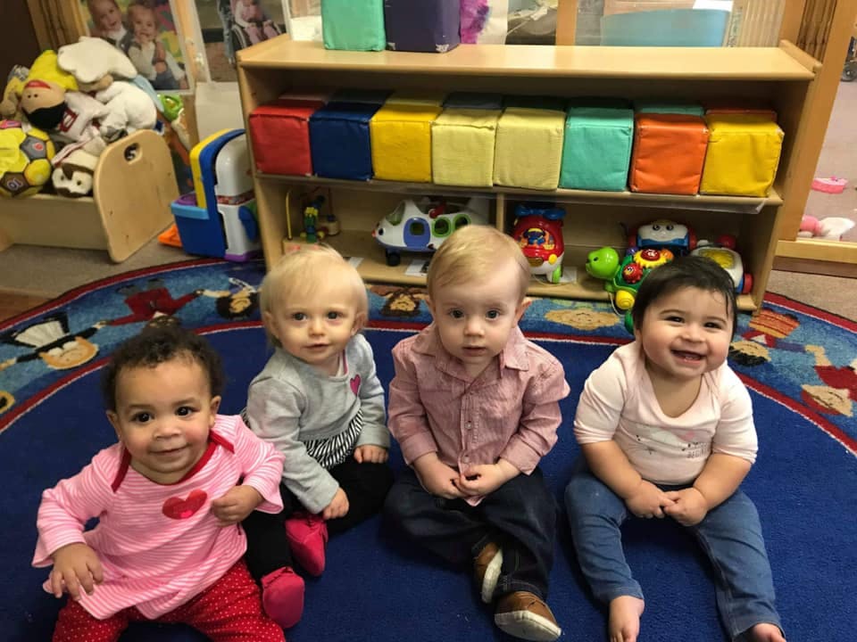 Four children sitting on a blue rug in a classroom