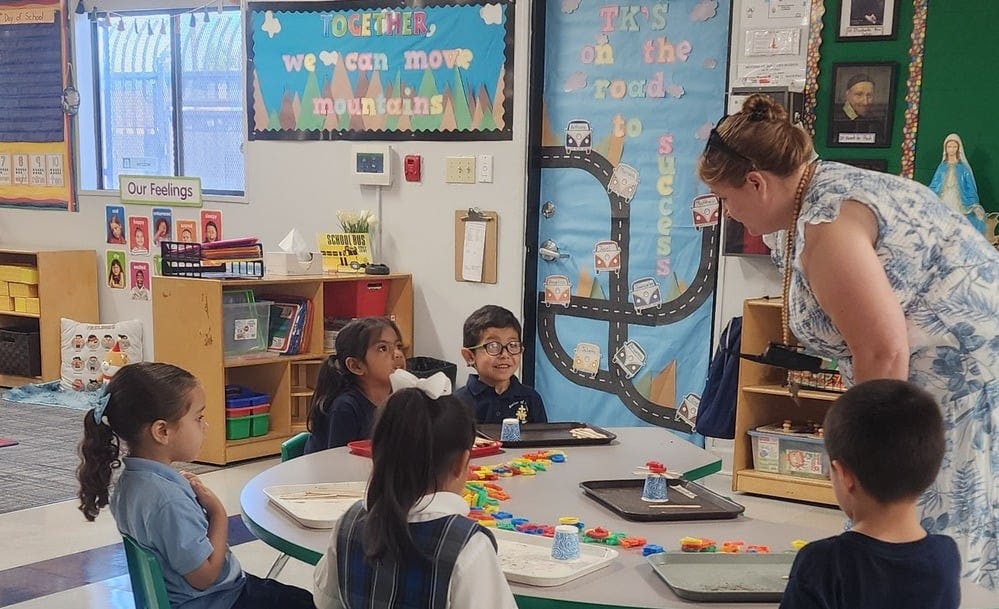 Teacher leaning over to supervise children at a table in a classroom