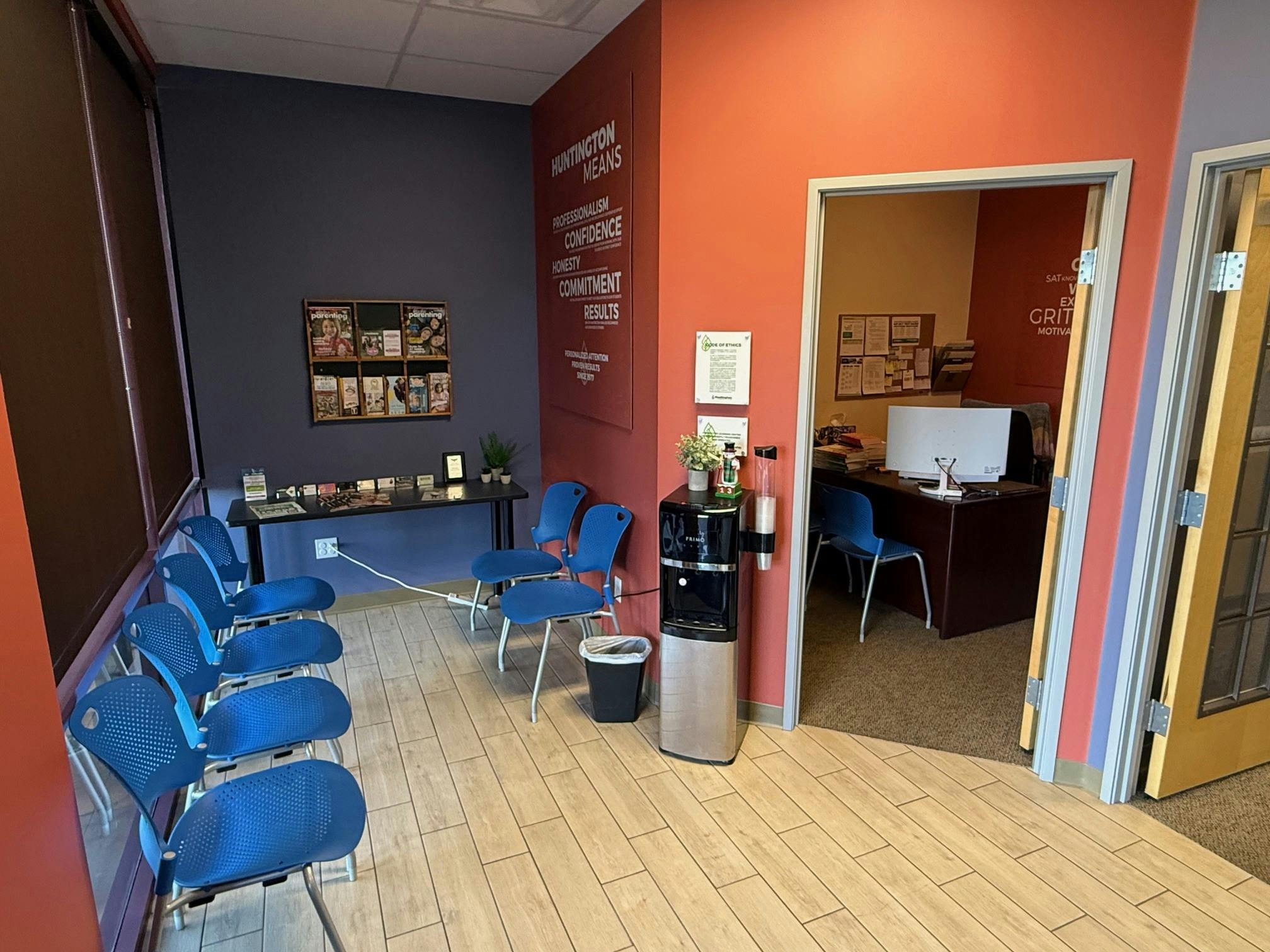 Waiting room with blue chairs, water cooler, and text on wall reading "Huntington Means"